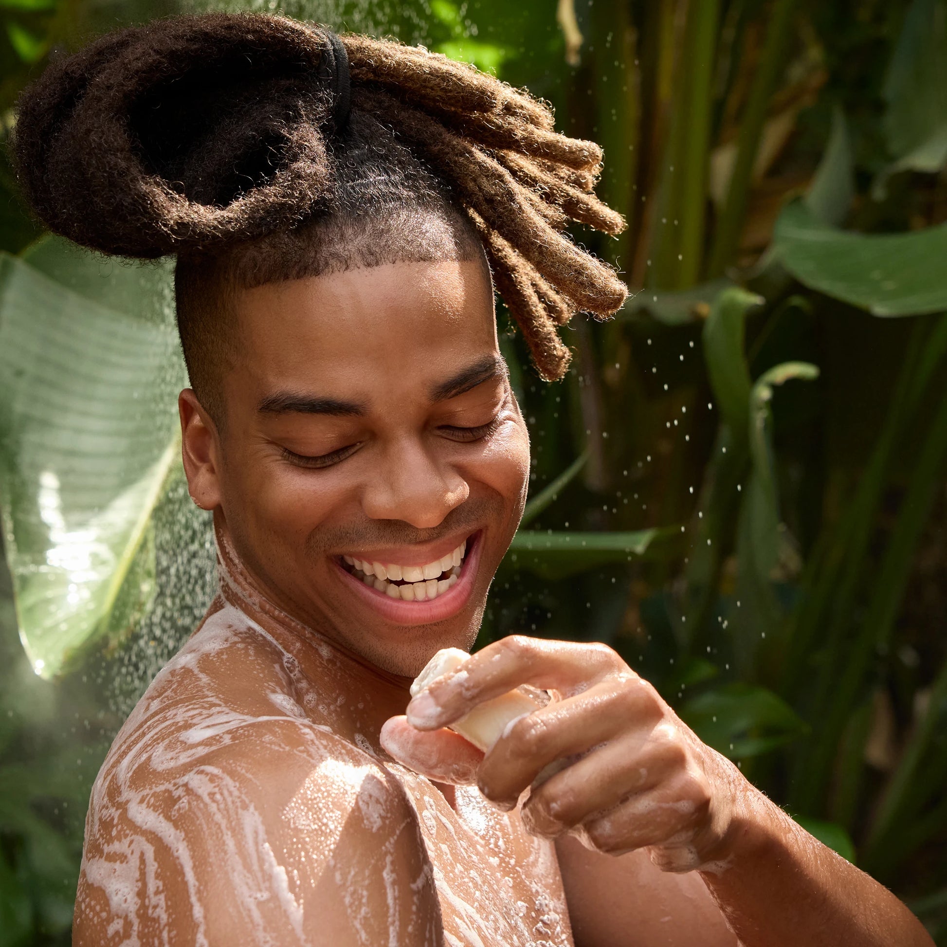 A person joyfully lathers soap on their shoulder, surrounded by lush green foliage. Ideal for promoting eco friendly, vegan, organic body wash or biodegradable soap in a natural setting [5 oz]