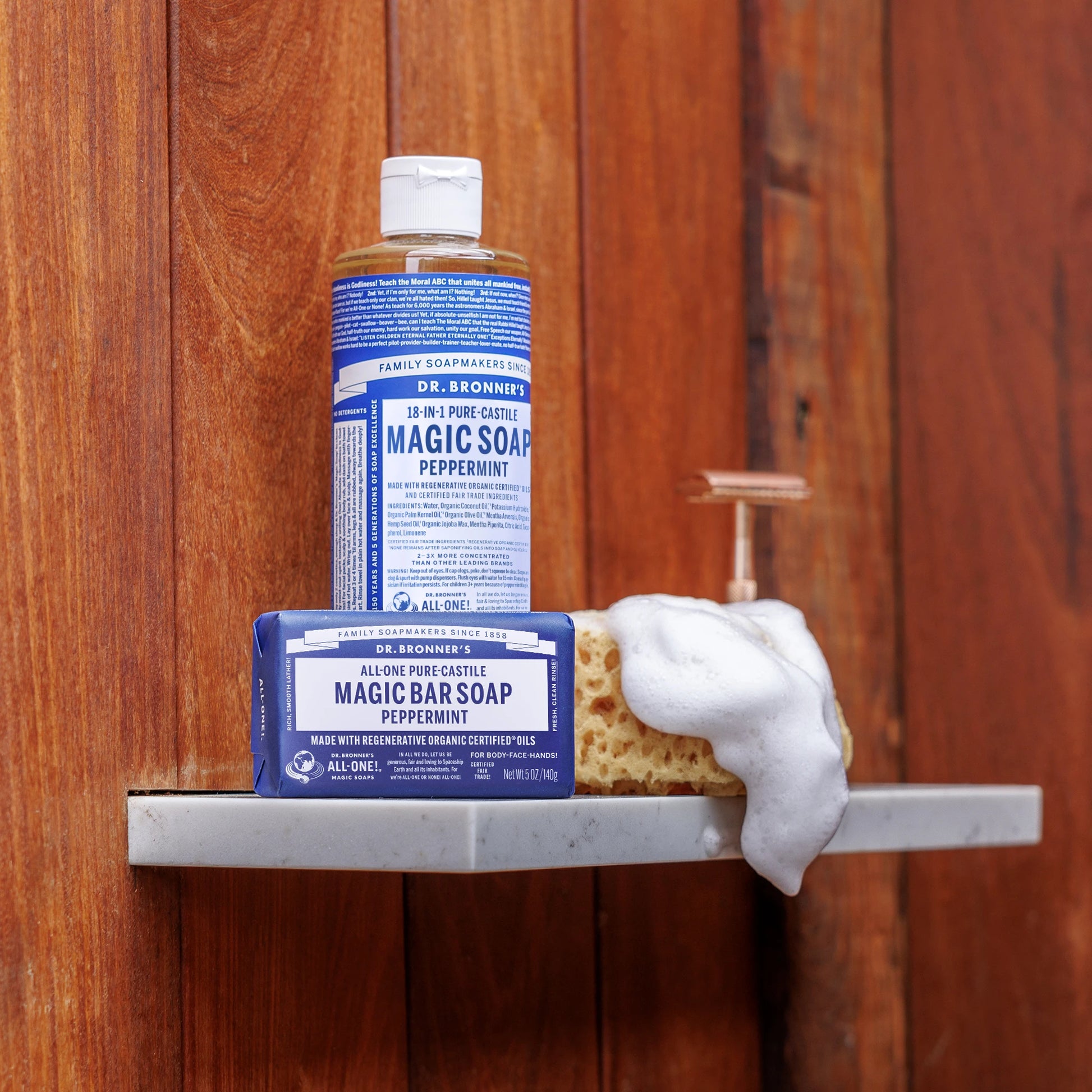 A bottle of Dr. Bronners Pure Castile Liquid Soap and a bar of soap sit on a shower shelf, surrounded by wood panel walls. Foam spills over an attached loofah, emphasizing cleanliness [5 oz]