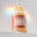 A gallon bottle of Dr. Bronners 18 in 1 Pure Castile Eucalyptus Soap stands on a tiled bathroom shelf, illuminated by a subtle rainbow light. Dr. Bronners Magic Soap Eucalyptus [1 Gallon]