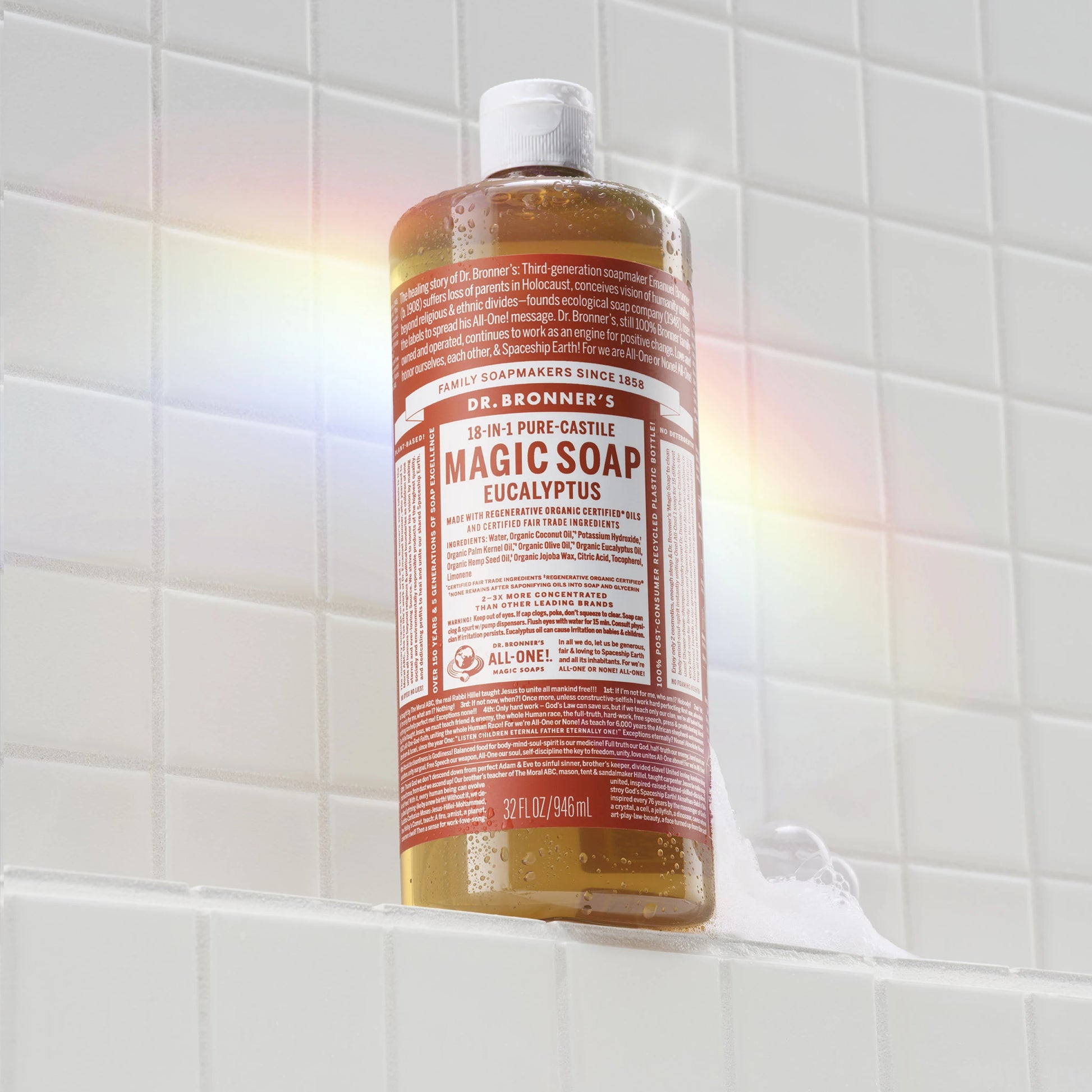 A bottle of Dr. Bronners rose castile soap rests on a white tiled surface. Sunlight creates a faint rainbow effect nearby, highlighting the natural, eco friendly product in a bathroom setting [32 oz]