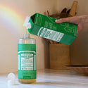 A hand pours Dr. Bronners Almond Pure Castile Liquid Soap into a bottle from a refill container, set on a white tiled surface with kitchen utensils in the background. Text includes MAGIC SOAP, ALMOND, Refill Refill Refill Ok and ALL ONE Keywords Dr. Bronners almond castile soap, liquid castile soap, biodegradable soap [32 oz]