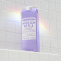 A lavender carton of Dr. Bronners Magic Soap Refill sits on a tiled bathroom shelf. A subtle rainbow reflection dances across the tiles, enhancing the soothing ambiance [32 oz]